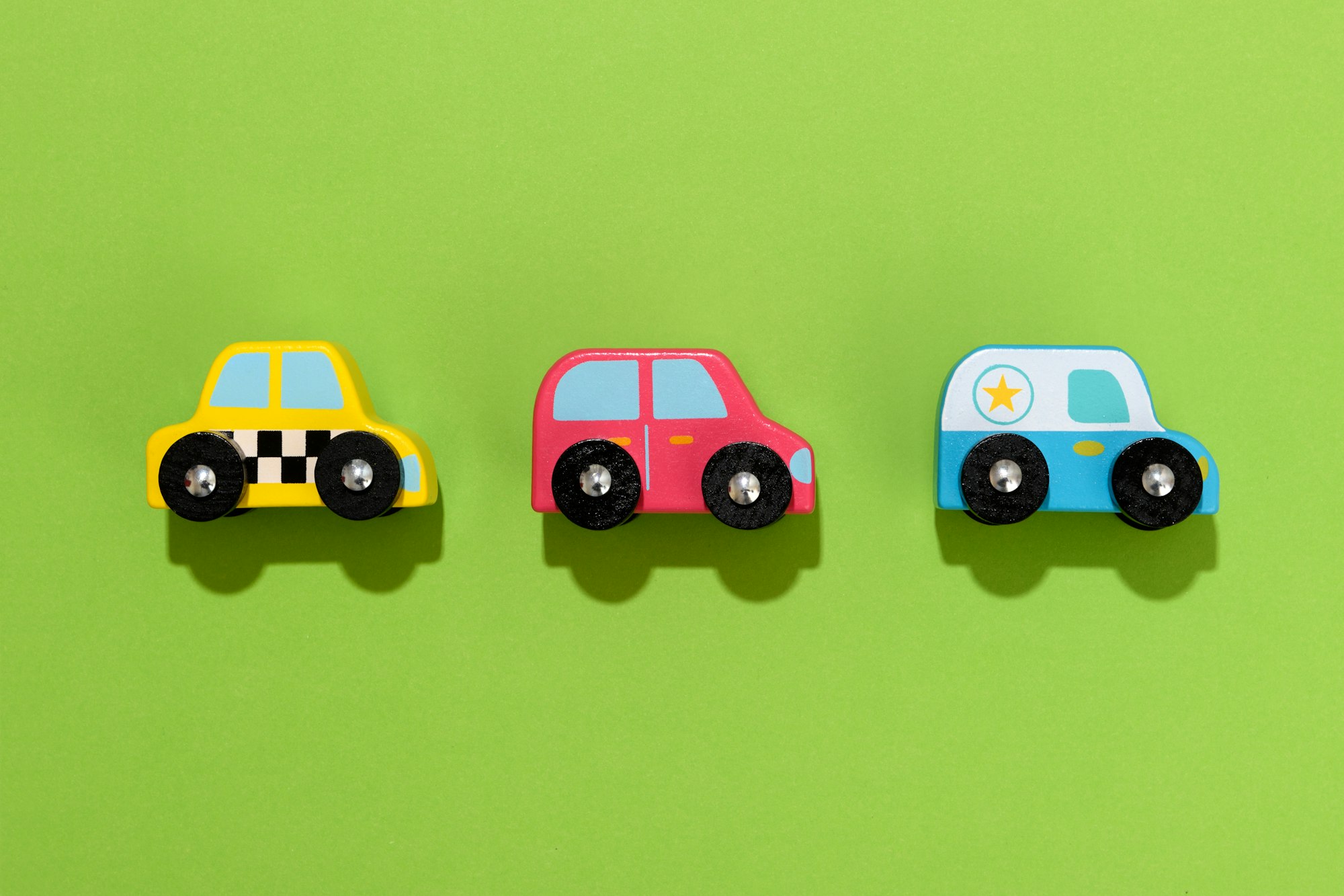 Three colorful wooden toy cars on green background